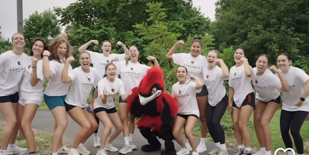 A red cardinal mascot poses with the volleyball team.